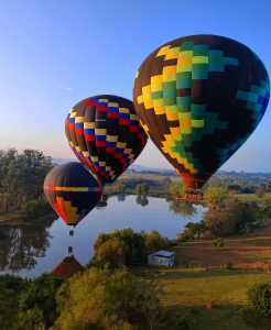 Três balões coloridos sobrevoando lagos e fazendas em Boituva ao amanhecer